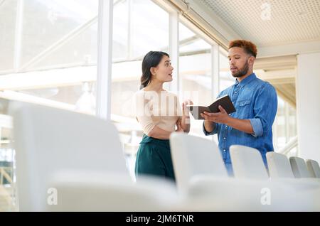 Working collaboratively towards big goals. two businesspeople going through a notebook together in an office. Stock Photo