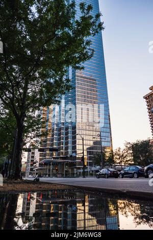 A high rise building and cars on the street with reflection on puddle water in Downtown Dallas Stock Photo