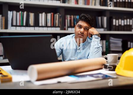 I think my career is having a mid life crisis. Portrait of a young architect looking bored while working at his desk in a modern office. Stock Photo
