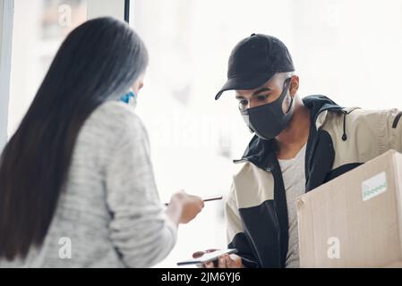 Contactless pay is for everybodys protection. a masked young man and woman using smartphones during a home delivery. Stock Photo