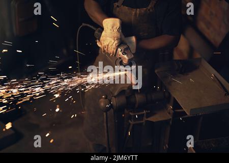 The steel industry is burning up. a man using an angle grinder while working at a foundry. Stock Photo
