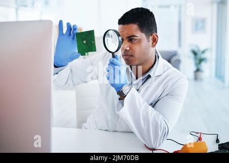 The most respected technician in the field. a young man using a magnifying glass while repairing computer hardware in a laboratory. Stock Photo