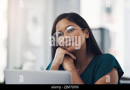 So many bright ideas are popping into her mind. a young businesswoman looking thoughtful while working on a laptop in an office. Stock Photo