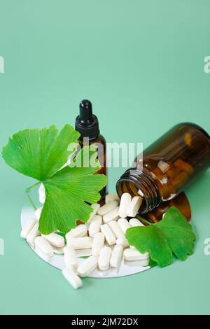 Ginkgo biloba pills.ginkgo biloba leaf and white tabletson green background.Preparations with ginkgo biloba extract.Alternative medicine and Stock Photo