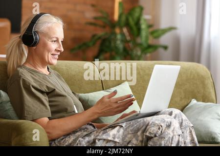 Mature female soldier in headphones using laptop at home Stock Photo