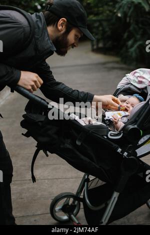 A father putting a pacifier in baby's mouth while pushing her in a stroller Stock Photo