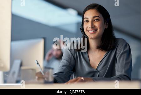 Build your client relationships, build your revenue. a young woman using a headset and computer late at night in a modern office. Stock Photo