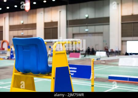 Blue chair of badminton referee with yellow colors near badminton net with blurred background in sport indoor stadium. Stock Photo