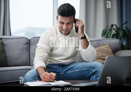 Stay home, smash goals. a young man using a laptop and smartphone while writing in a notebook at home. Stock Photo