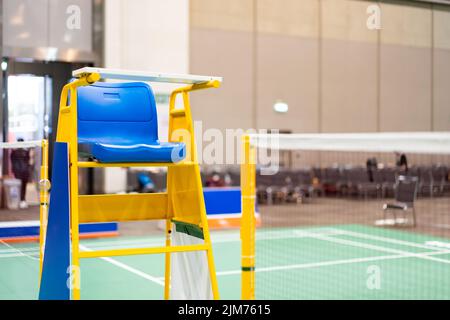 Blue chair of badminton referee with yellow colors near badminton net with blurred background in sport indoor stadium. Stock Photo