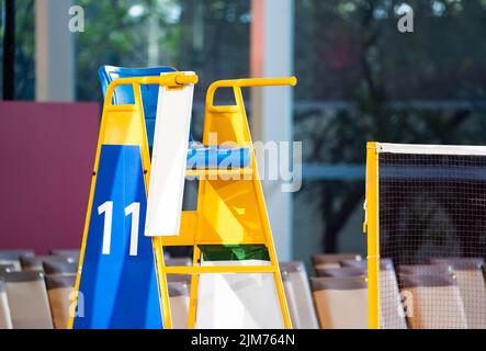 Blue chair of badminton referee with yellow colors near badminton net with blurred background in sport indoor stadium. Stock Photo