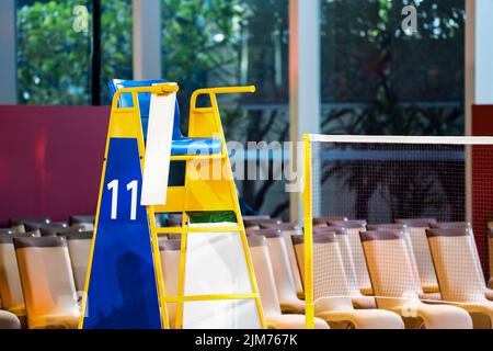 Blue chair of badminton referee with yellow colors near badminton net with blurred background in sport indoor stadium. Stock Photo