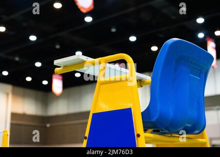 Blue chair of badminton referee with yellow colors near badminton net with blurred background in sport indoor stadium. Stock Photo