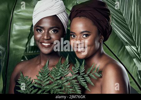 Together is a good place to be. Studio portrait of two beautiful young women posing in front of palm leaves against a grey background. Stock Photo