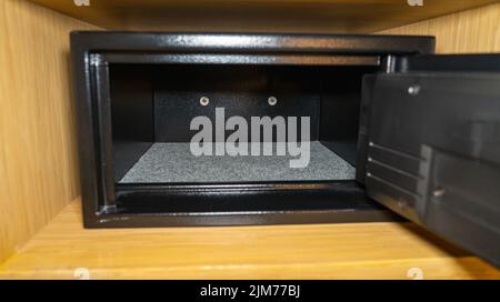 An open black empty safe with its door open in a wooden shelf. Stock Photo