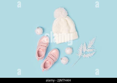 White knitted hat and pink sneakers on blue background. Winter set of child clothes. Fashion kids outfit. Top view Flat lay. Stock Photo