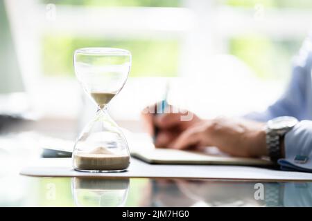 Close-up Of Hourglass In Front Of Businessperson's Hand Calculating Invoice Stock Photo