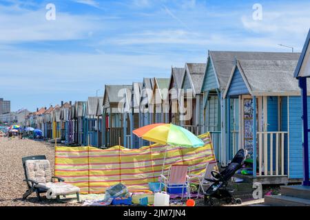 Herne Bay, Kent, UK - August 3 2022: Vibrant beach huts, beach umbrellas and deckchairs on the beach during a locally hot August day in 2022. Stock Photo