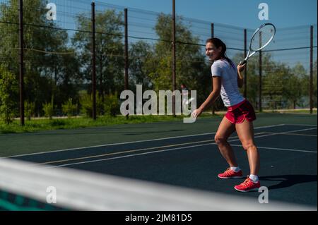 Young caucasian woman playing tennis on an outdoor court on a hot summer day. Stock Photo