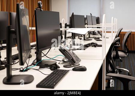 Office space with PC monitors, phones and headsets on the tables. Coworking area, empty call center, corporate business Stock Photo