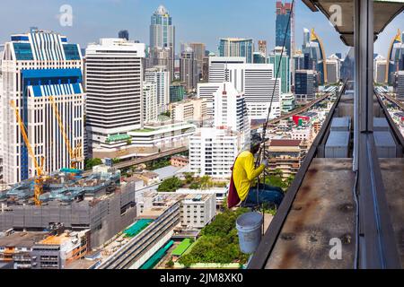 Thai workman repairing window in high rise building using rope and pulley, Bangkok, Thailand Stock Photo