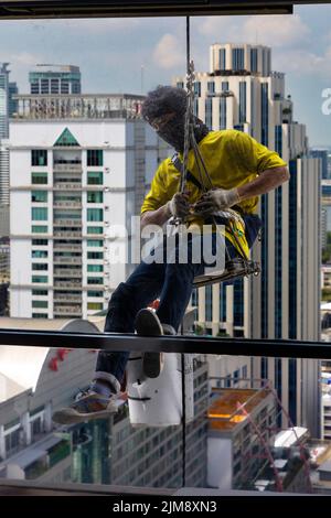Thai workman repairing window in high rise building using rope and ...