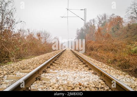 Scenic view of straight railway or railroad track receding into distance on foggy day. The concept of traveling by train. Stock Photo