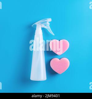 Cleaning spray bottle with two pink heart shaped sponges on blue background. Top view. Stock Photo