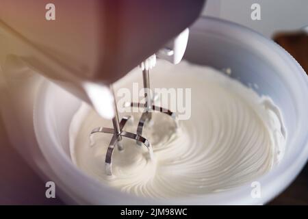Mixing white egg cream in bowl with motor mixer. Baking cake. Whipped cream and mixer. Stock Photo