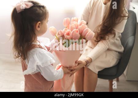 Happy mother's day! Child daughter congratulates moms and gives her pink flowers tulips. Stock Photo