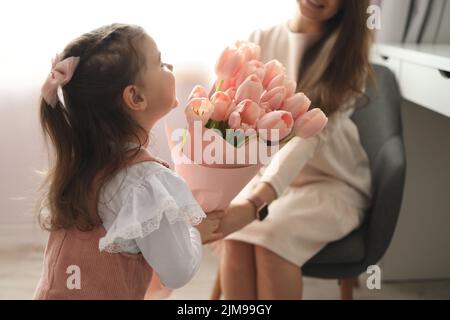 Happy mother's day! Child daughter congratulates moms and gives her pink flowers tulips. Stock Photo
