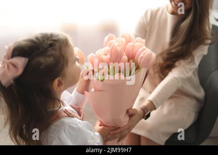 Happy mother's day! Child daughter congratulates moms and gives her pink flowers tulips. Stock Photo