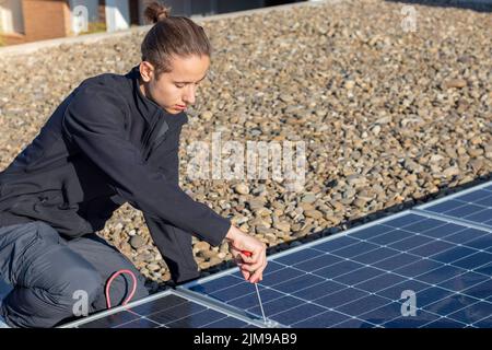 Concentrated young man worker with bun hairstyle screwing and assembling new solar apnels for eco solar energy source Stock Photo