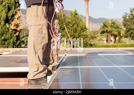Cropped view of young woman working as electrician with red wire hanging in a solar panel installation job Stock Photo