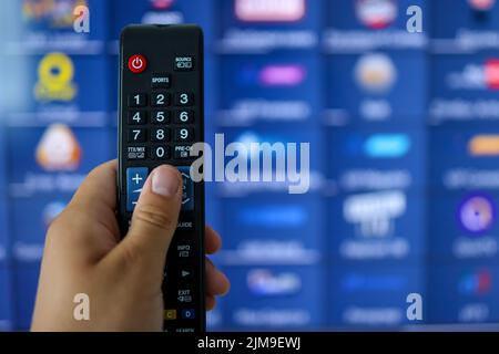 Smart tv and hand pressing remote control. Hand holding TV remote control with a television in the background. Close up. Stock Photo