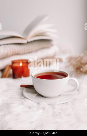 A cup of tea on the window with burning candles and sweaters. Stock Photo