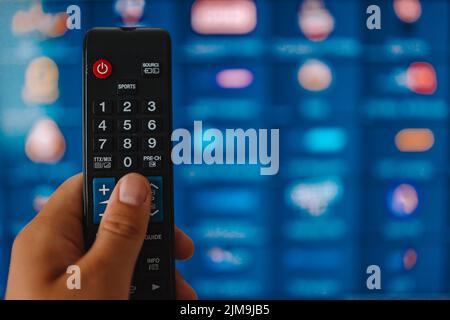 Smart tv and hand pressing remote control. Hand holding TV remote control with a television in the background. Close up. Stock Photo