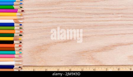Colorful pencils lined up along with ruler on oak wooden desktop Stock Photo
