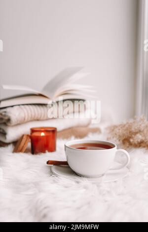 A cup of tea on the window with burning candles and sweaters. Stock Photo