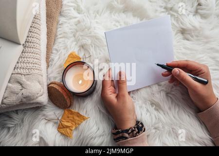 The girl writes a letter on the background of a candle. Home comfort. Stock Photo