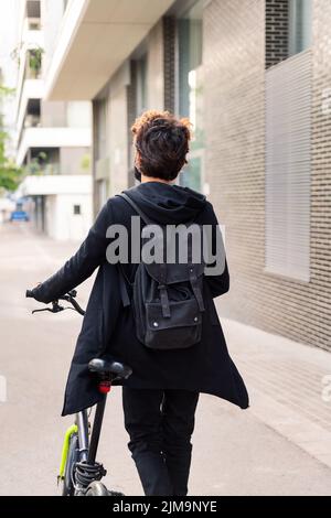 rear view of an unrecognizable young man walking with his bike, concept of urban lifestyle and sustainable mobility Stock Photo