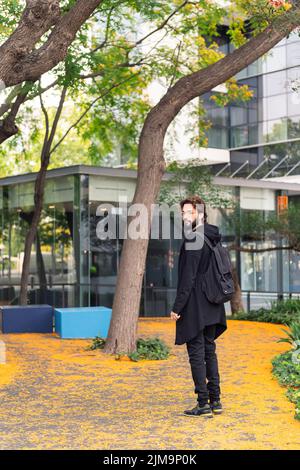 stylish college student with backpack walking by the park of the university campus, concept of youth and education, copy space for text Stock Photo