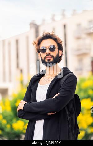 stylish young man with beard and sunglasses posing outdoors with arms crossed looking at camera, concept of youth and urban life style, copy space for Stock Photo