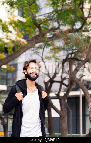 smiling college student with backpack walking happy by the park of the university campus, concept of youth and education, copy space for text Stock Photo