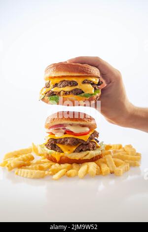 Hand holding a gourmet cheese burger on top of another beef burger with potato chips on the bottom Stock Photo