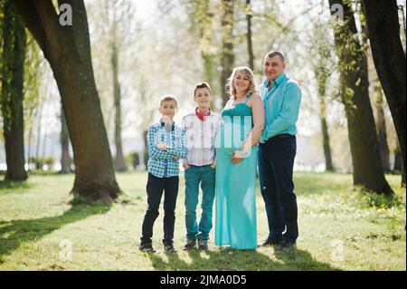 Portrait of happy pregnant family with two sons, dressed in a turquoise clothes at park Stock Photo