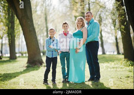 Portrait of happy pregnant family with two sons, dressed in a turquoise clothes at park Stock Photo