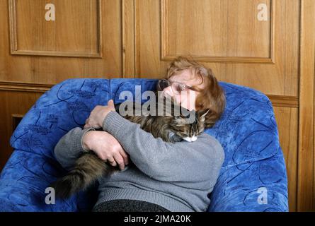 Old woman asleep in a chair in an embrace with a cat Stock Photo