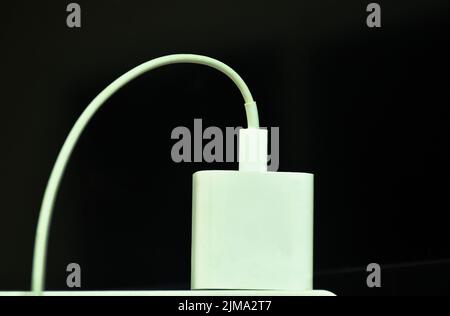 white mobile phone charger stabbing in plug in socket on black background Stock Photo