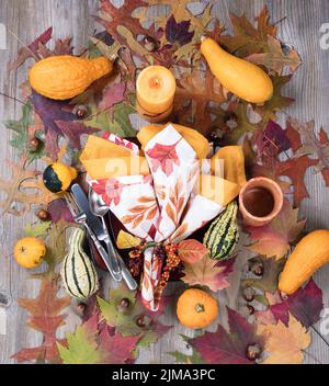 Dinner setting for fall season with burning candle plus real gourd decorations and leaves on rustic wooden boards Stock Photo